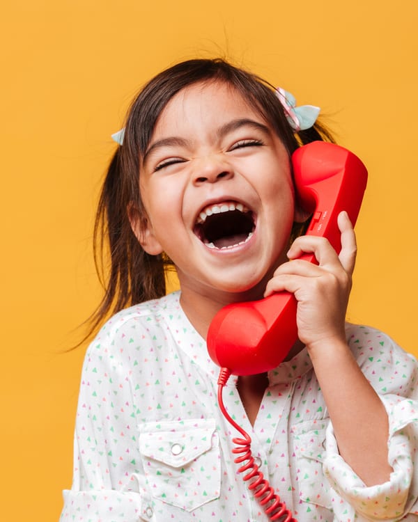 Girl laughing as she talks on a red telephone